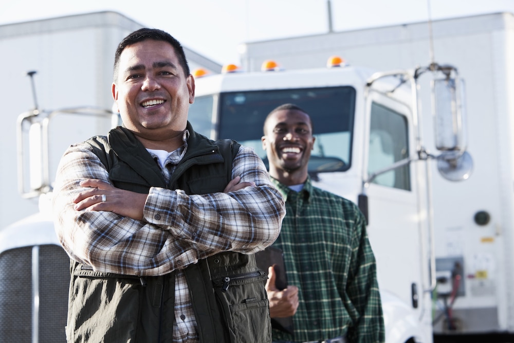 Two fleet workers stand in front of a truck